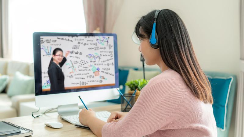 Female student working at home desk with instructor on desktop computer screen